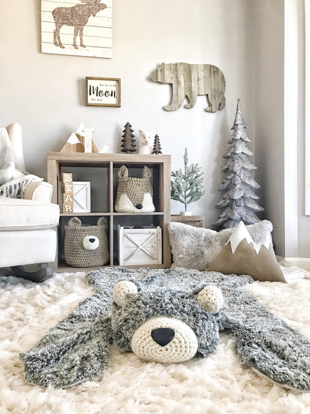 An adventure theme nursery with a plush gray bear rug made by ClaraLoo on the floor. A bear basket and fox basket made by ClaraLoo are on shelves in the background.